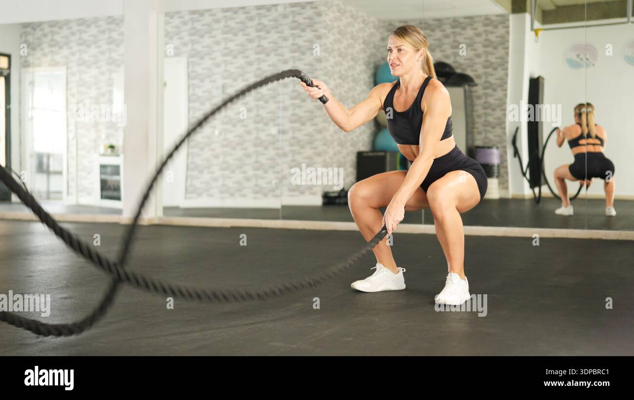 Femme exerçant avec des cordes de combat dans le squatting de gymnastique pour la forme physique Banque D'Images