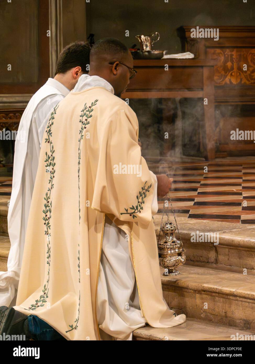 Crémone, Italie 2 février 2026 prêtre en vêtements ornés agenouillé dans l'allée de la cathédrale, balançant thurible avec de l'encens pendant la liturgie catholique solennelle Banque D'Images