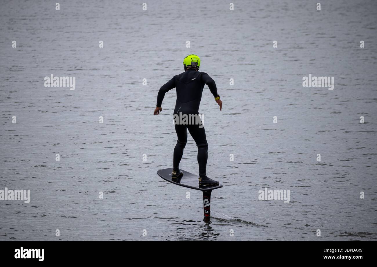 Cavalier en combinaison noire et casque balance sur e-foil alors qu'il se soulève de l'eau à West Kirby Banque D'Images