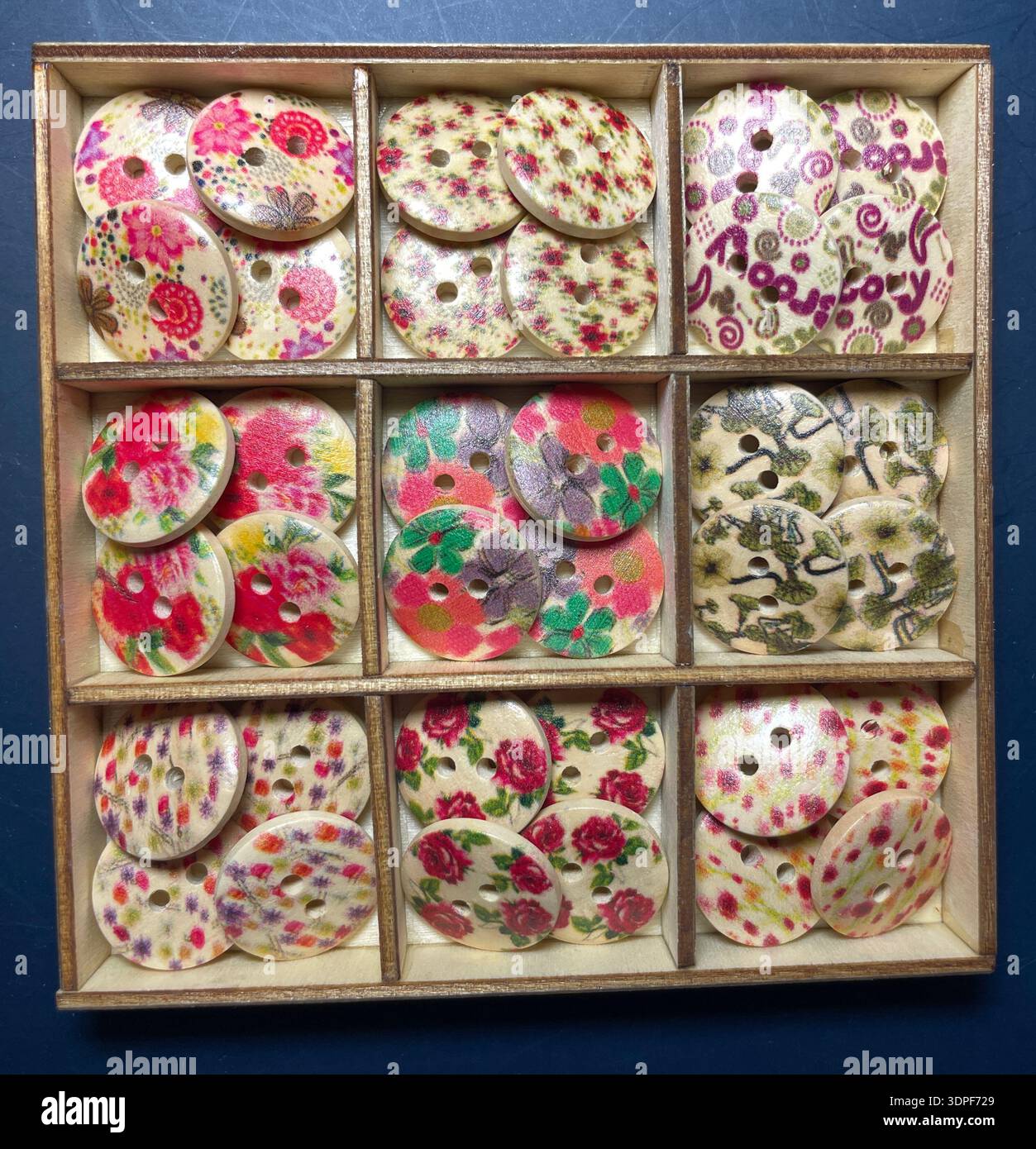 Assortiment de charmants boutons en bois vintage dans un plateau en bois avec des motifs floraux romantiques, des roses, des marguerites et des motifs botaniques Banque D'Images