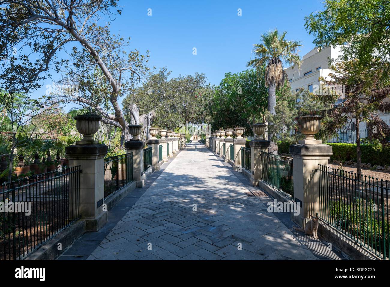 Chemin pavé bordé d'arbres dans les jardins botaniques d'Argotti, la Valette, avec des balustrades en pierre, des jardinières décoratives d'urne et des garde-corps en fer sous un soleil d'été lumineux Banque D'Images