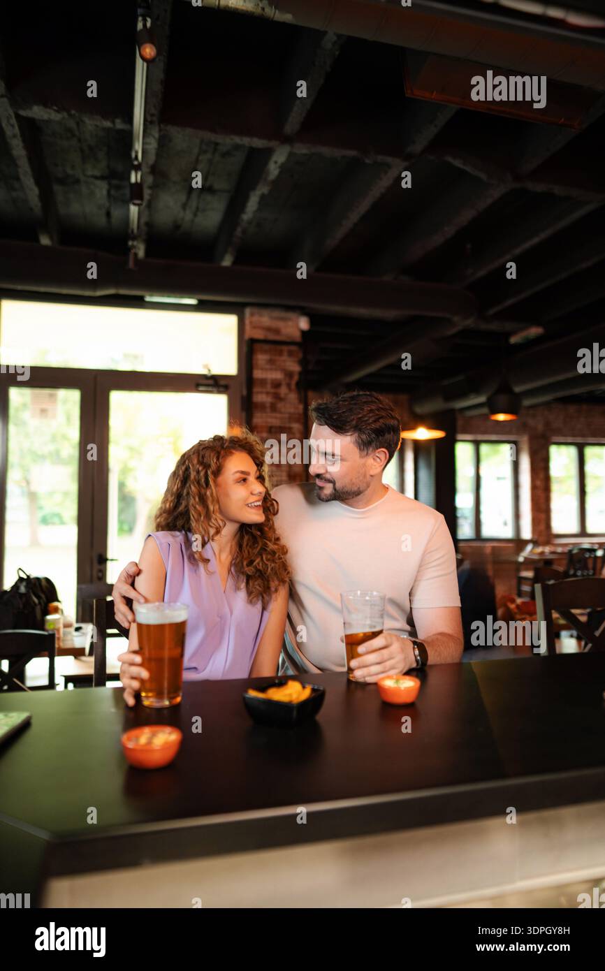 Couple profitant de la bière et des collations au comptoir du bar dans un pub Banque D'Images