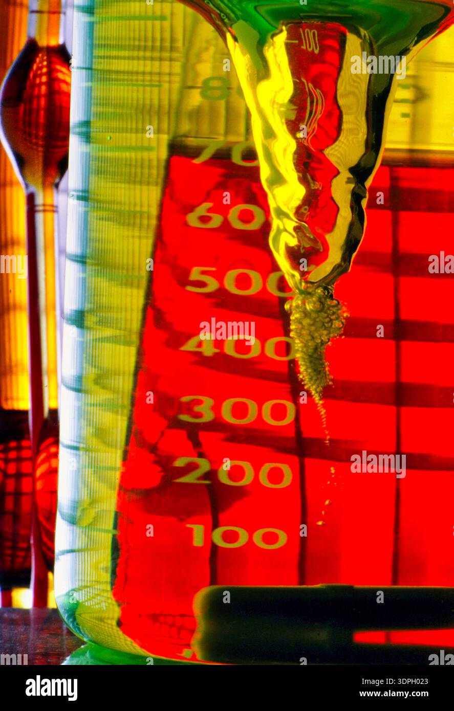 Un bécher de laboratoire montre des liquides colorés se mélangeant et créant des bulles. L'échelle du bécher affiche les mesures. La lumière joue à travers les liquides Banque D'Images