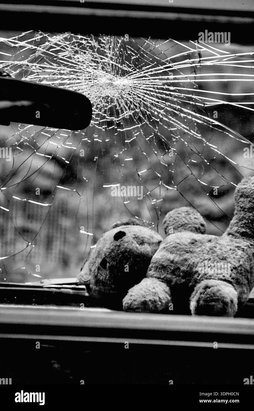 Photo noir et blanc d'un ours en peluche d'enfant repose sur le siège avant d'une voiture bleue. Le pare-brise est fissuré et cassé après une collision Banque D'Images