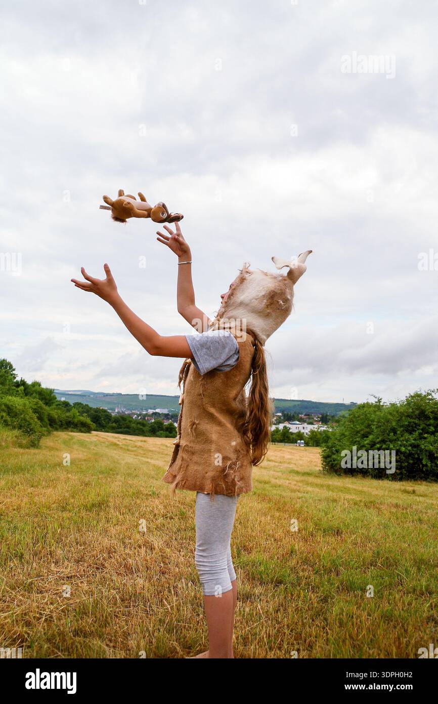 Fille en costume de lapin et chapeau avec de longues oreilles, jouant avec le jouet en peluche dans le champ sous le ciel nuageux Banque D'Images