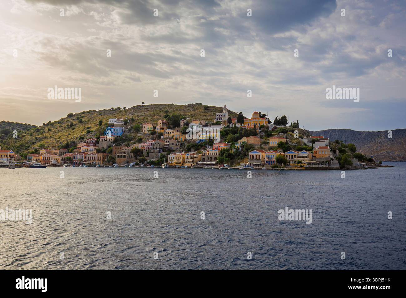 Bâtiments colorés sur une colline dans la ville idyllique de Symi au bord de la mer Égée sur l'île de Symi (Simi, Syme) en Grèce par un jour nuageux. Banque D'Images