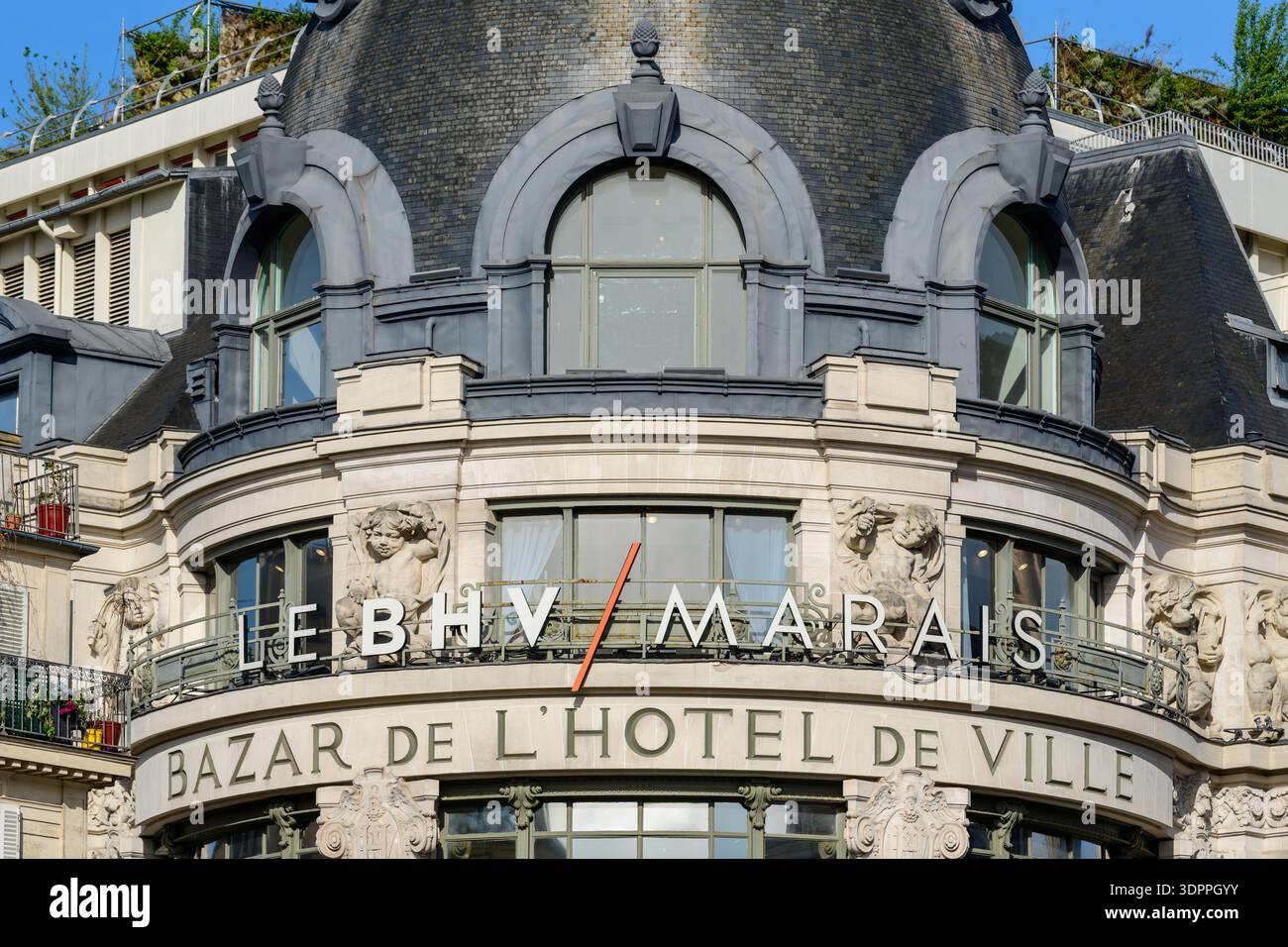 Paris, France - 27 avril 2022 : la façade supérieure du grand magasin le BHV Marais est visible, avec de grandes fenêtres cintrées, des sculptures décoratives en pierre et des enseignes marquantes indiquant « LE BHV/MARAIS » et « BAZAR DE L'HÔTEL DE VILLE ». Banque D'Images