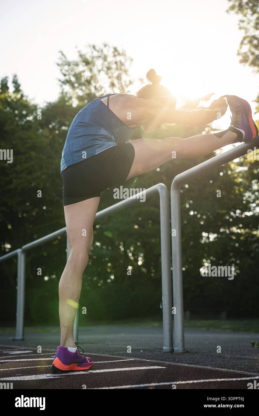 Femme étire la jambe sur les balustrades entourées d'arbres et de lumière du soleil, coureuse de fond moyenne Katharina Jaiser, Gechingen, Allemagne Banque D'Images