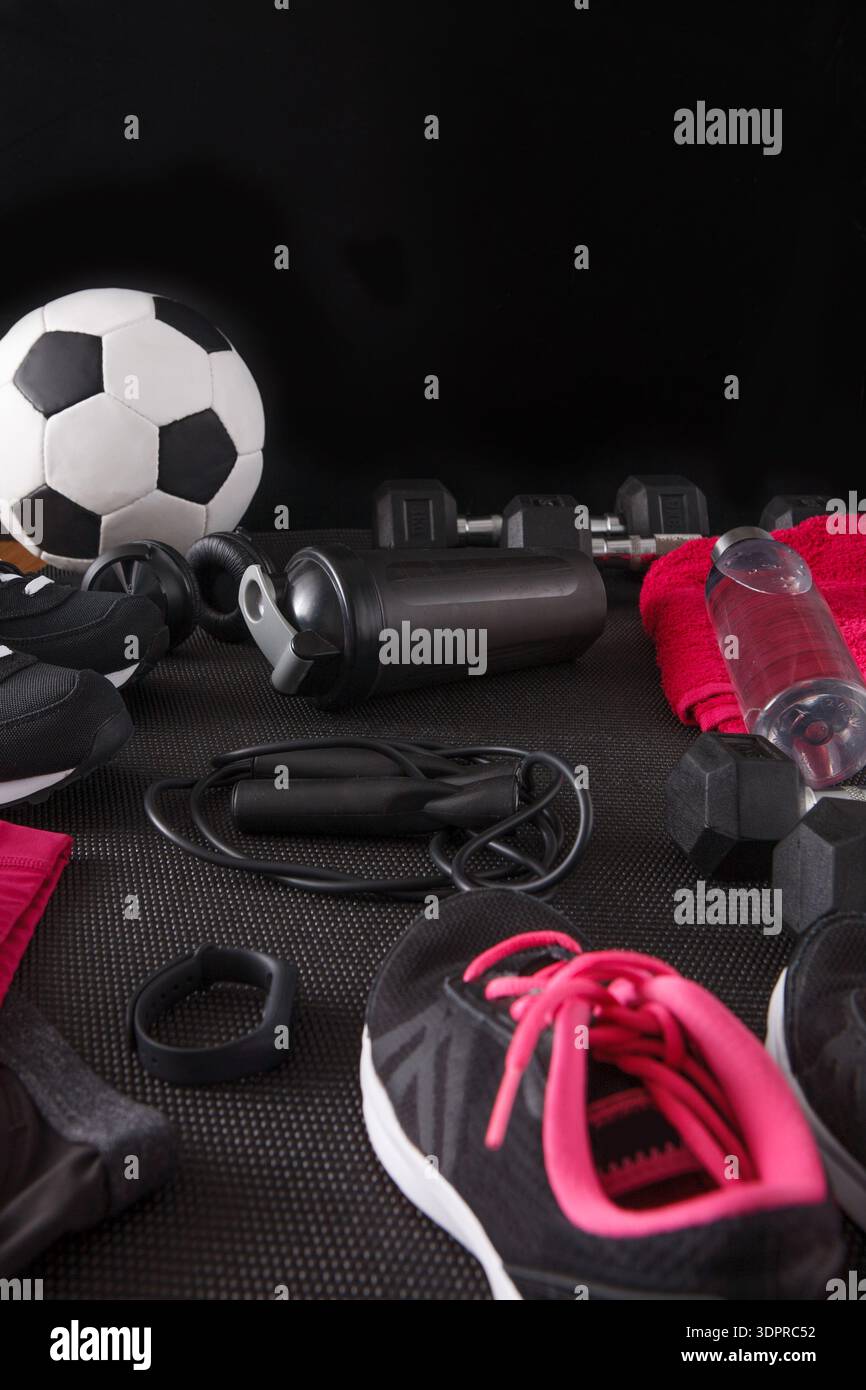 Équipement pour les sports et les entraînements disposés sur fond noir avec ballon de football et poids Banque D'Images