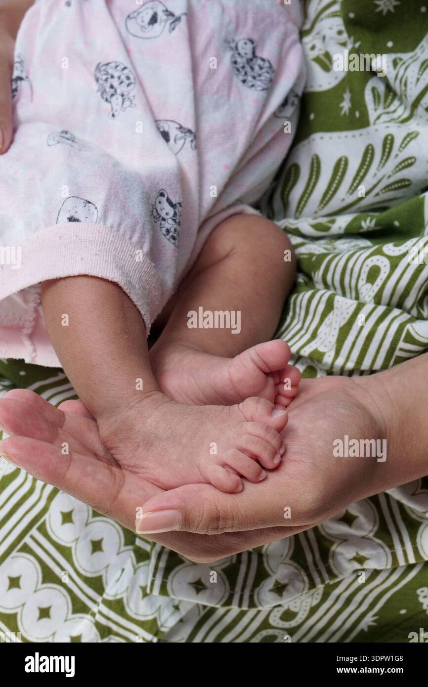 Photo intime et en grand angle montrant la main d'un adulte berçant les pieds délicats d'un bébé. Le contraste de taille souligne la tendresse du pari obligataire Banque D'Images