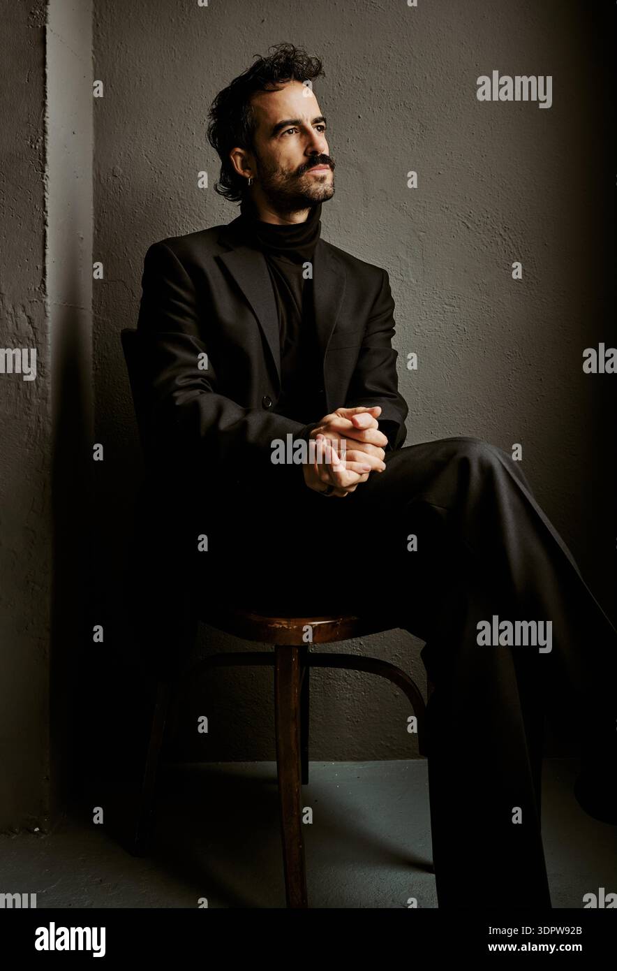 Homme pensif en costume noir assis seul dans des ombres dramatiques Banque D'Images