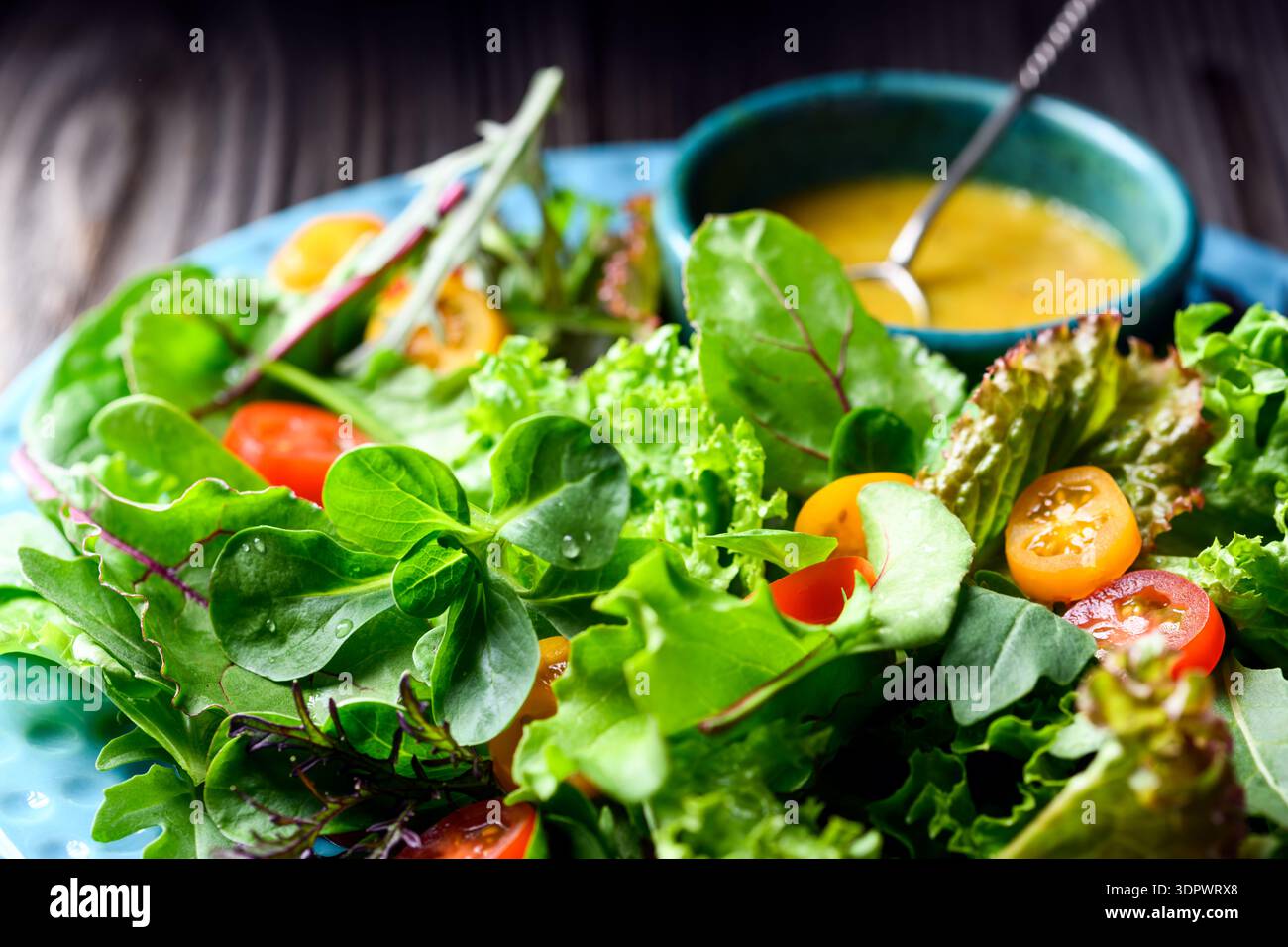 Salades vertes mélangées avec tomates cerises et vinaigrette sur table en bois, mélange de laitue fraîche. Style alimentaire naturel Banque D'Images