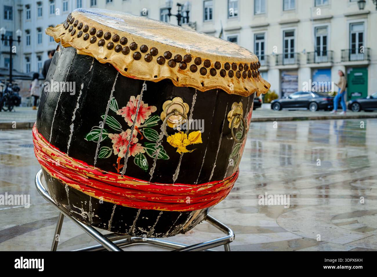 9 février 2024 - Lisbonne, Portugal : tambour chinois traditionnel en bois et en cuir altérés sur la place de la ville européenne, trottoir humide et reflets de bâtiment, pendant les célébrations du nouvel an lunaire. Diversité culturelle, multiculturalisme, intégration de la diaspora, Asie Banque D'Images