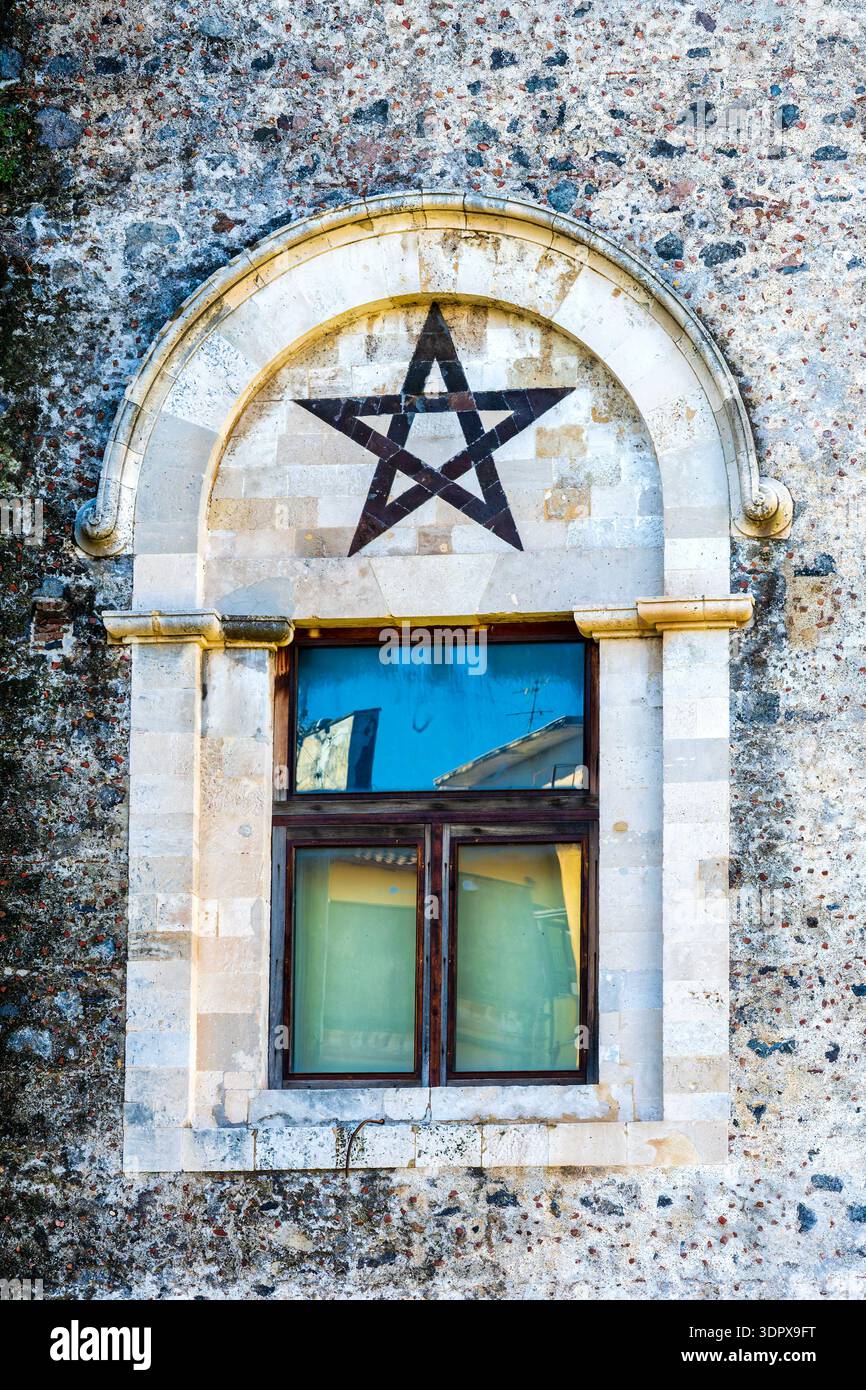 Gros plan de l'étoile à cinq branches en pierre de lave noire (pentagramme) au-dessus du tympan de fenêtre voûtée sur le mur est de Castello Ursino, Catane, Sicile, Italie Banque D'Images