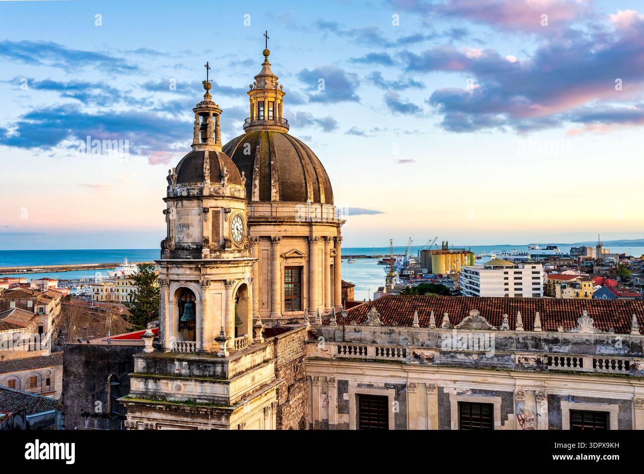 Dôme et clocher de la Cattedrale di Sant’Agata à Catane, Sicile, Italie, vue au coucher du soleil avec mer et port en arrière-plan. Banque D'Images