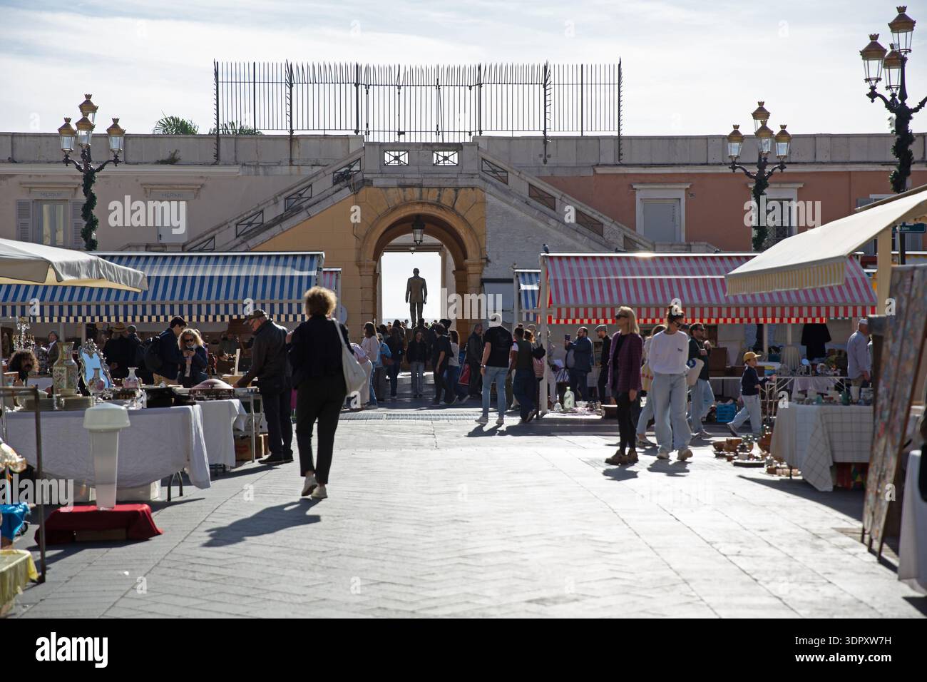 Marché aux puces à Nice, dans le sud de la France, avec des stands rayés, des acheteurs en plein air et une architecture historique sous une lumière méditerranéenne claire. Banque D'Images