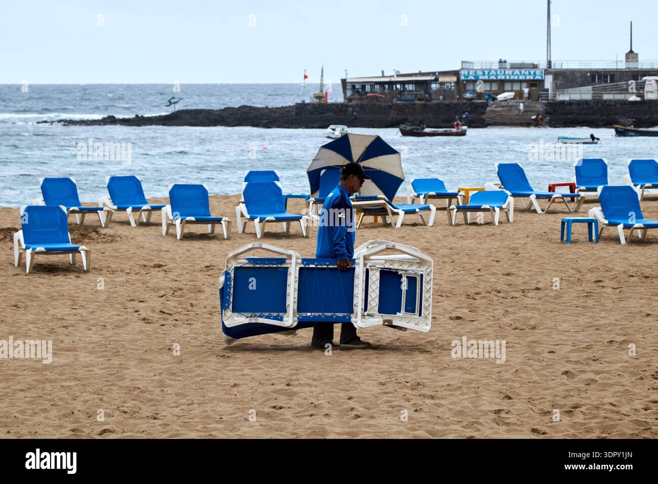 homme emballant chaises de plage et parasols à la fin de la journée playa de las canteras las palmas de gran canaria, îles canaries, espagne Banque D'Images