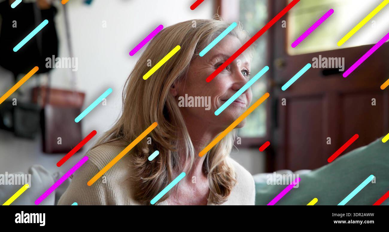 Femme mature souriante portant un pull en tricot léger assis sur un canapé, stries multicolores superposées Banque D'Images