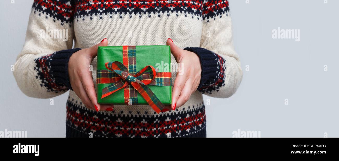 Cadeau de vacances présenté par une personne dans un pull en tricot lors d'un rassemblement festif Banque D'Images