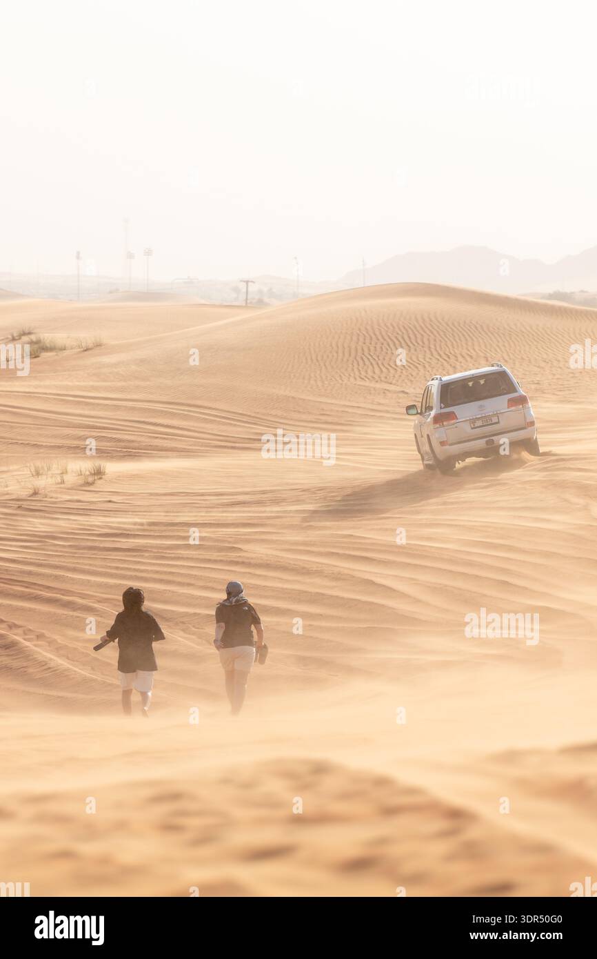 Dubaï, Émirats Arabes Unis-9 mars 2025 : véritable exploration du désert comme 4x4 hors route grimpant les dunes de sable et les touristes marchant en dessous, scène immersive pour Banque D'Images