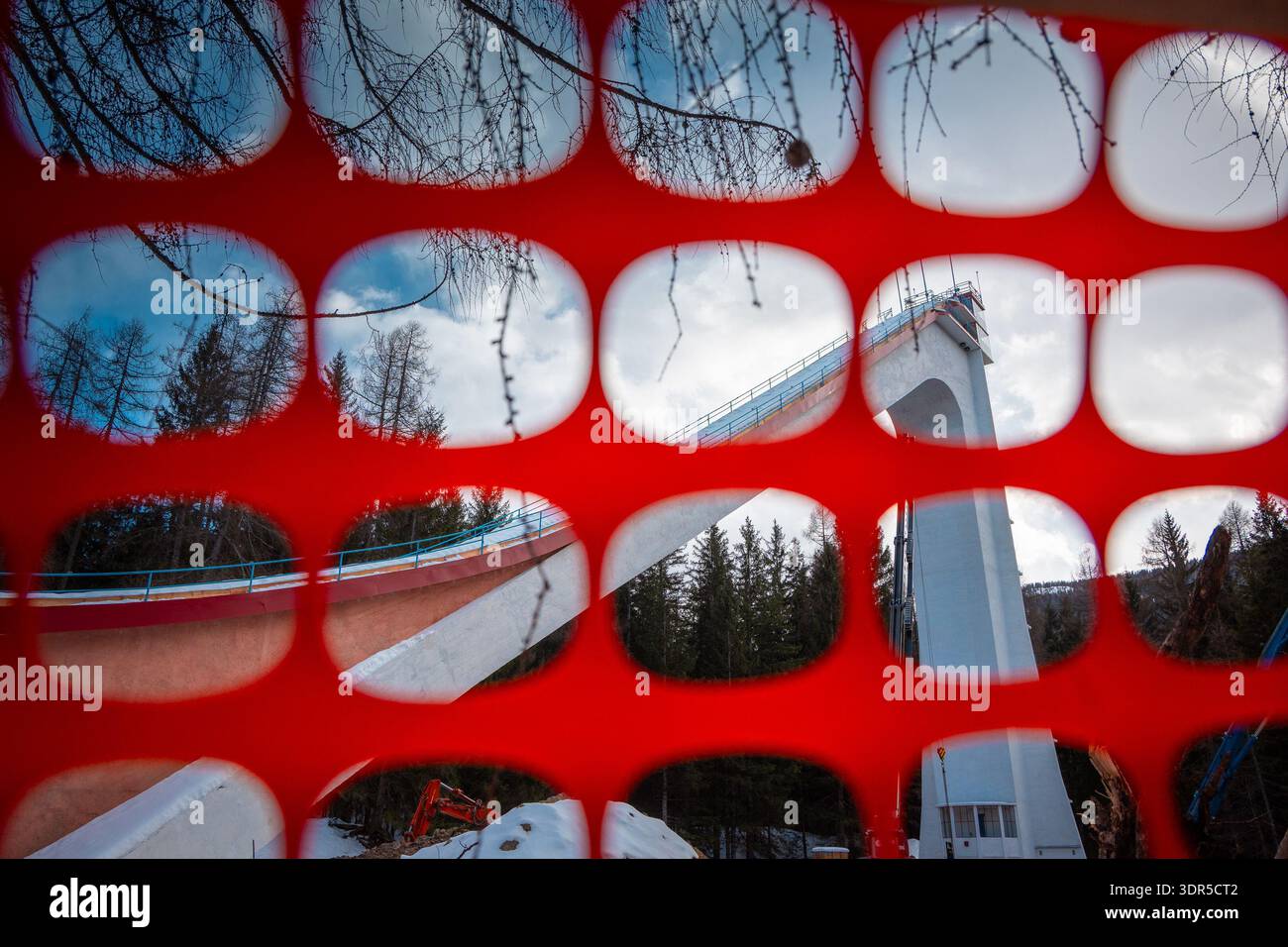 Tour de saut à ski à Cortina d Ampezzo vue à travers le filet de sécurité rouge, créant un cadre géométrique audacieux avec des arbres alpins, structure en béton, hiver Banque D'Images