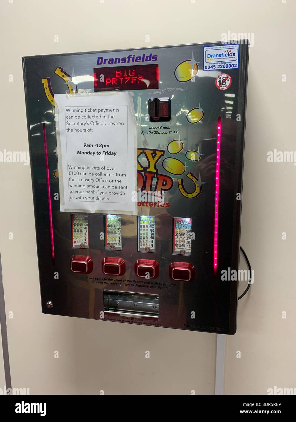 Distributeur automatique de loteries Lucky Dip de Dransfield's avec panneaux lumineux et plusieurs distributeurs de billets avec un avis expliquant la collecte des prix - Image de stock capturée avec un smartphone