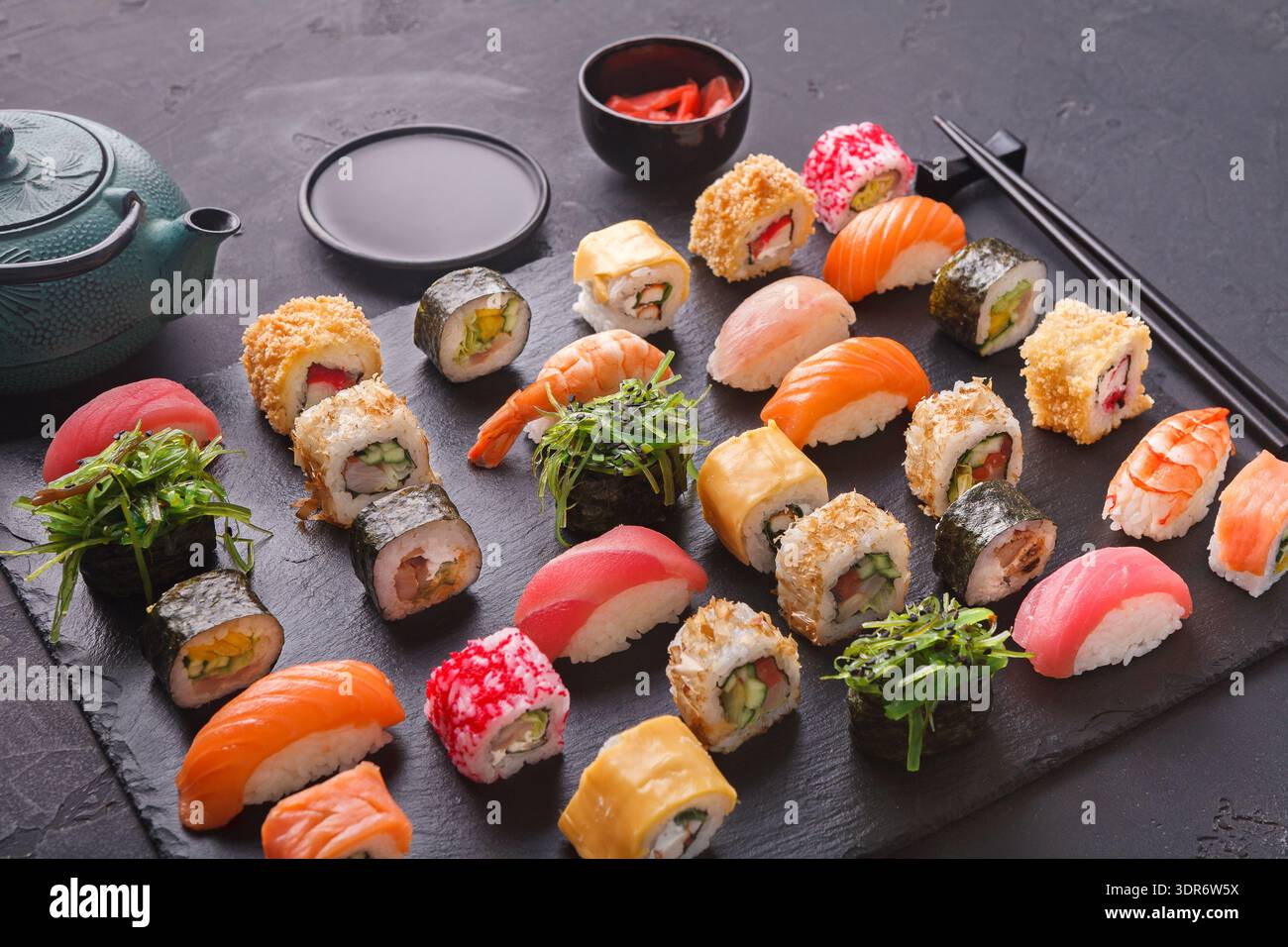 Collection de Sushi Rolls sur un plateau en pierre noire avec thé et gingembre mariné Banque D'Images