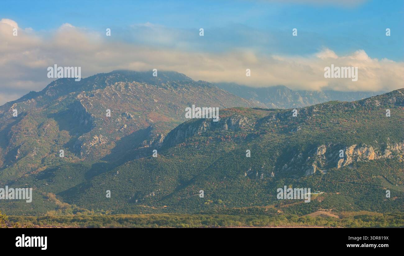 Vue imprenable sur les montagnes en couches couvertes d'une végétation luxuriante et d'affleurements rocheux, avec des nuages doux dérivant à travers le ciel bleu Banque D'Images