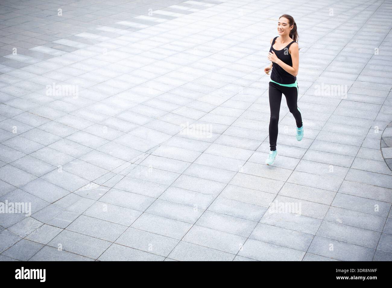 Courir sur un chemin pavé pendant la journée dans un cadre urbain avec des baskets bleues et des vêtements d'entraînement Banque D'Images