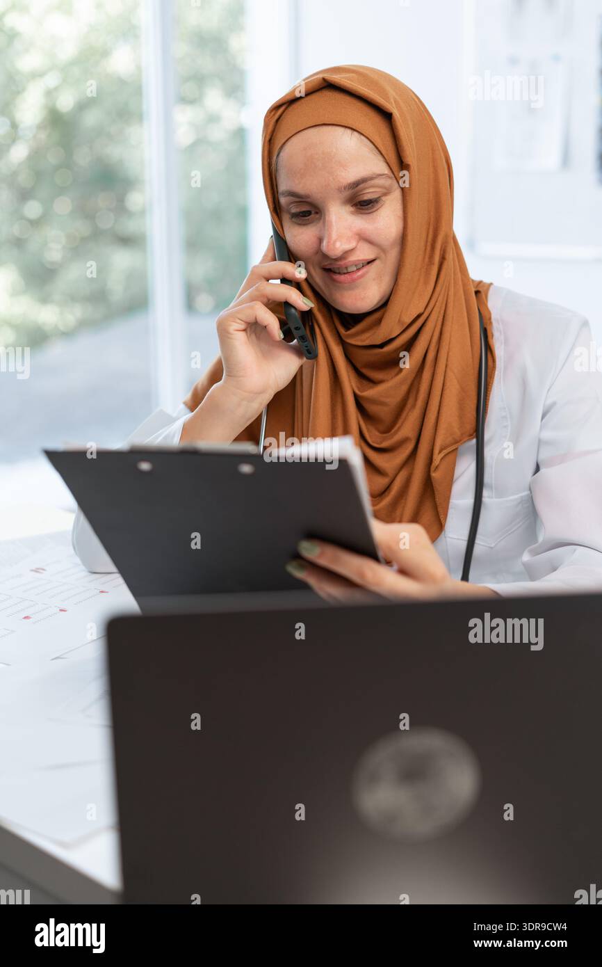 Médecin féminin arabe fournit des conseils médicaux en utilisant le téléphone travaillant dans la clinique moderne. consultations de patients. Banque D'Images