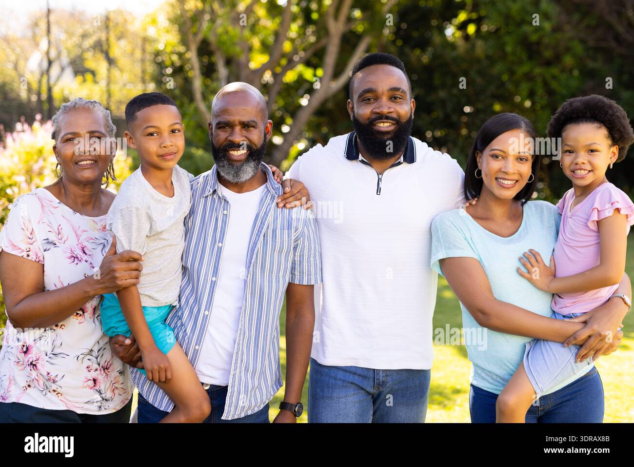 Debout ensemble et souriant, famille multi-générationnelle dans le jardin ensoleillé en plein air Banque D'Images