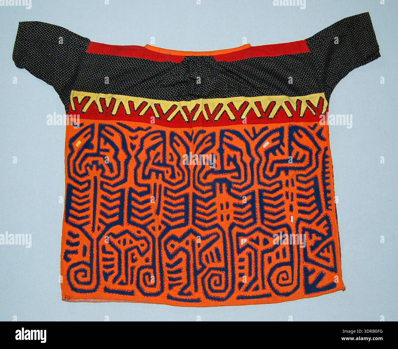 Chemisier mola du début du XXe siècle en coton. Empiècement en coton noir imprimé avec des carrés blancs et des lignes bleues ; coton rouge sur les épaules ; coton orange cousu autour du cou. Bande de rouge et jaune vs appliquéd en bas de l'empiècement. Dos du corps en coton rouge avec des points verts. Motif appliqué central orange et bleu représentant des scorpions. Illustre la construction textile, la superposition, la technique appliquée, la combinaison de couleurs, le motif géométrique, expression culturelle, et compétence artistique du peuple Kuna. Banque D'Images