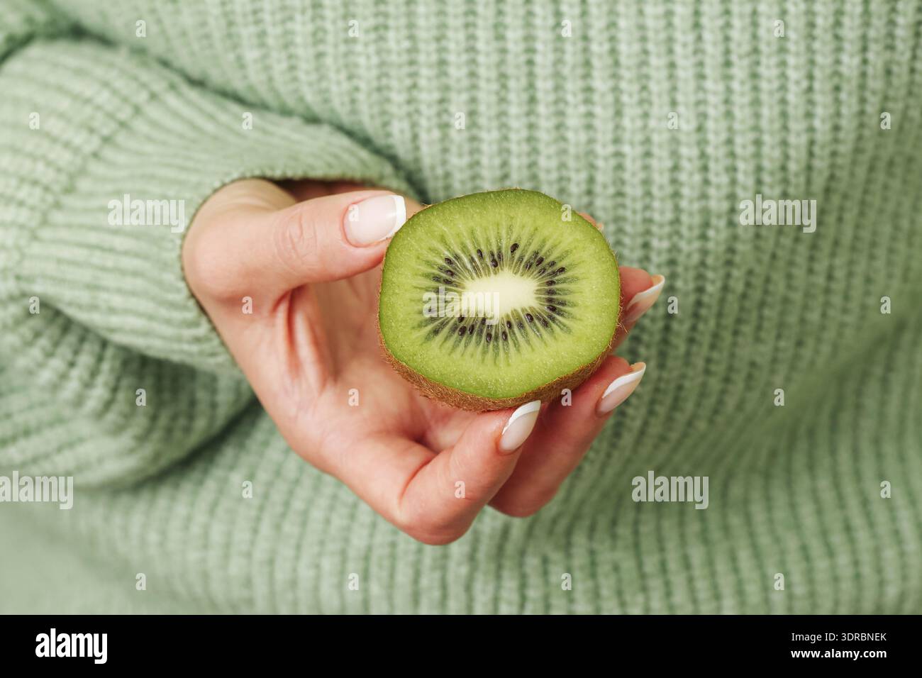 Femme tenant le kiwi tranché gros plan. Concept de nourriture fraîche saine. Ingrédient tropical vert et source naturelle de vitamines à l'intérieur. Banque D'Images
