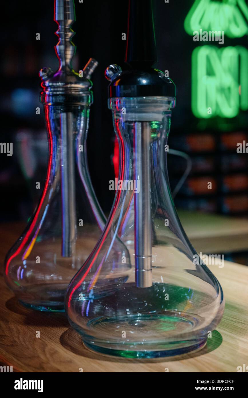 Deux hookahs en verre modernes sur un support en bois dans un intérieur sombre avec éclairage au néon.hookahs professionnels assemblés contre un mur de briques et néon vert dedans Banque D'Images