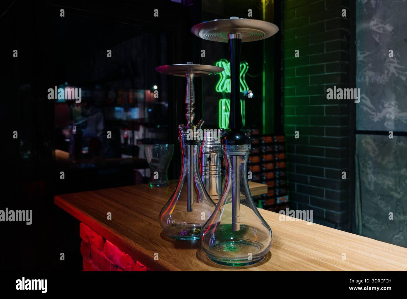 Deux hookahs en verre modernes sur un support en bois dans un intérieur sombre avec éclairage au néon.hookahs professionnels assemblés contre un mur de briques et néon vert dedans Banque D'Images