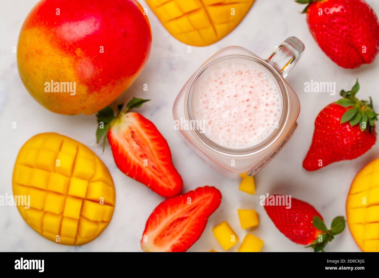 Smoothie ou milkshake à base de fraises fraîches, mangue, yaourt ou lait et glaçons dans un pot Mason sur une table en marbre. Concept Banque D'Images