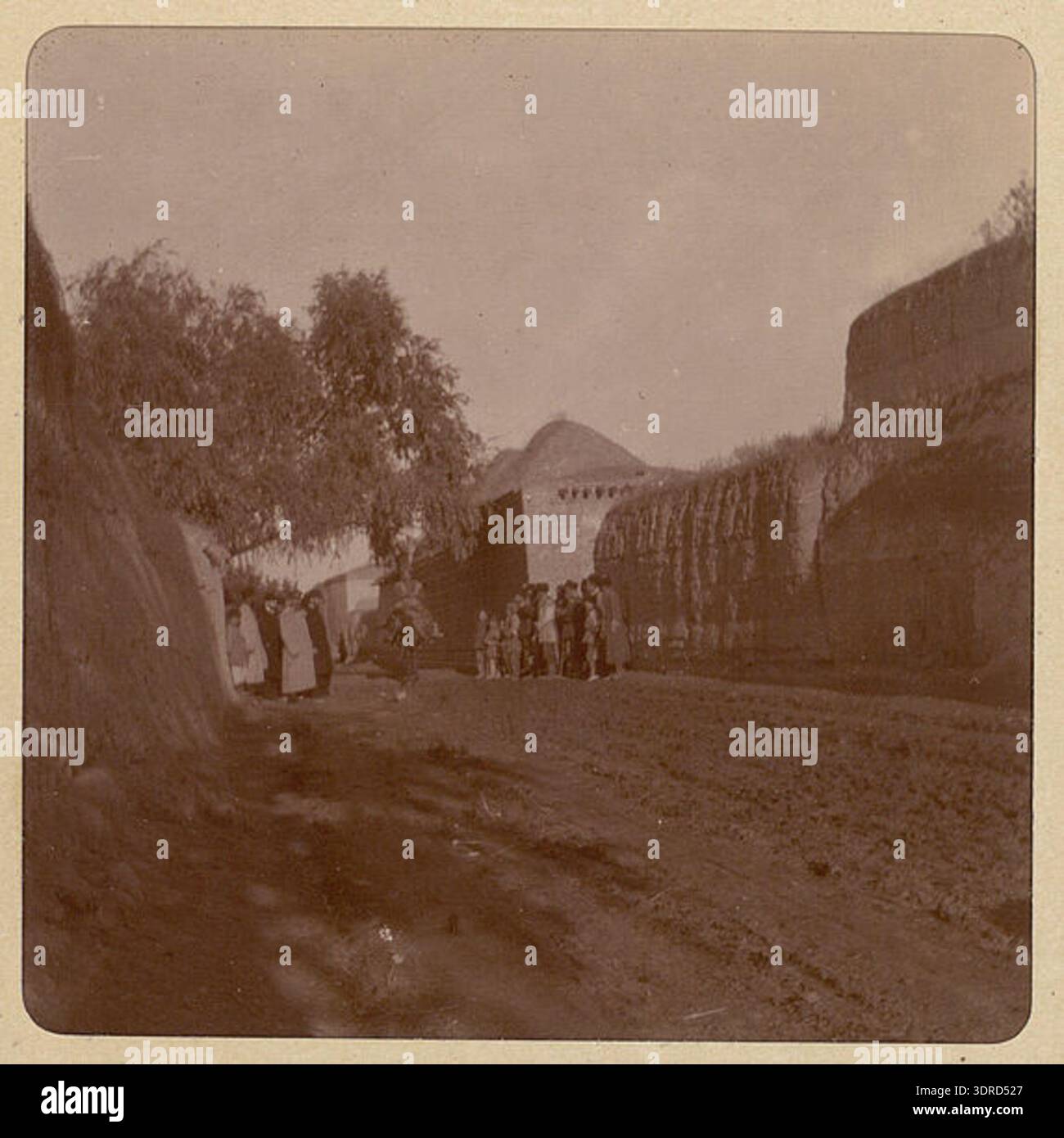 Cette photographie de 1900 de Joseph de Baye représente la vue de rue d'une maison ensoleillée située rue Nizami, allée 5, maison 33, à Ganja, Azerbaïdjan. L'image montre l'architecture résidentielle urbaine, le tracé des rues, les effets de la lumière du soleil, les détails des fenêtres et du toit, et les conditions de vie domestiques dans les villes azerbaïdjanaises du début du XXe siècle, donnant un aperçu de la culture urbaine locale et du logement. Banque D'Images