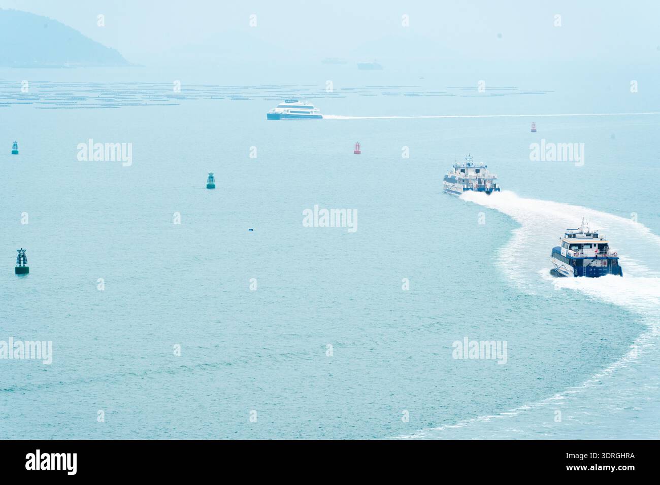Bateaux rapides naviguant dans les eaux côtières avec des bouées et une masse terrestre lointaine sous ciel brumeux Banque D'Images