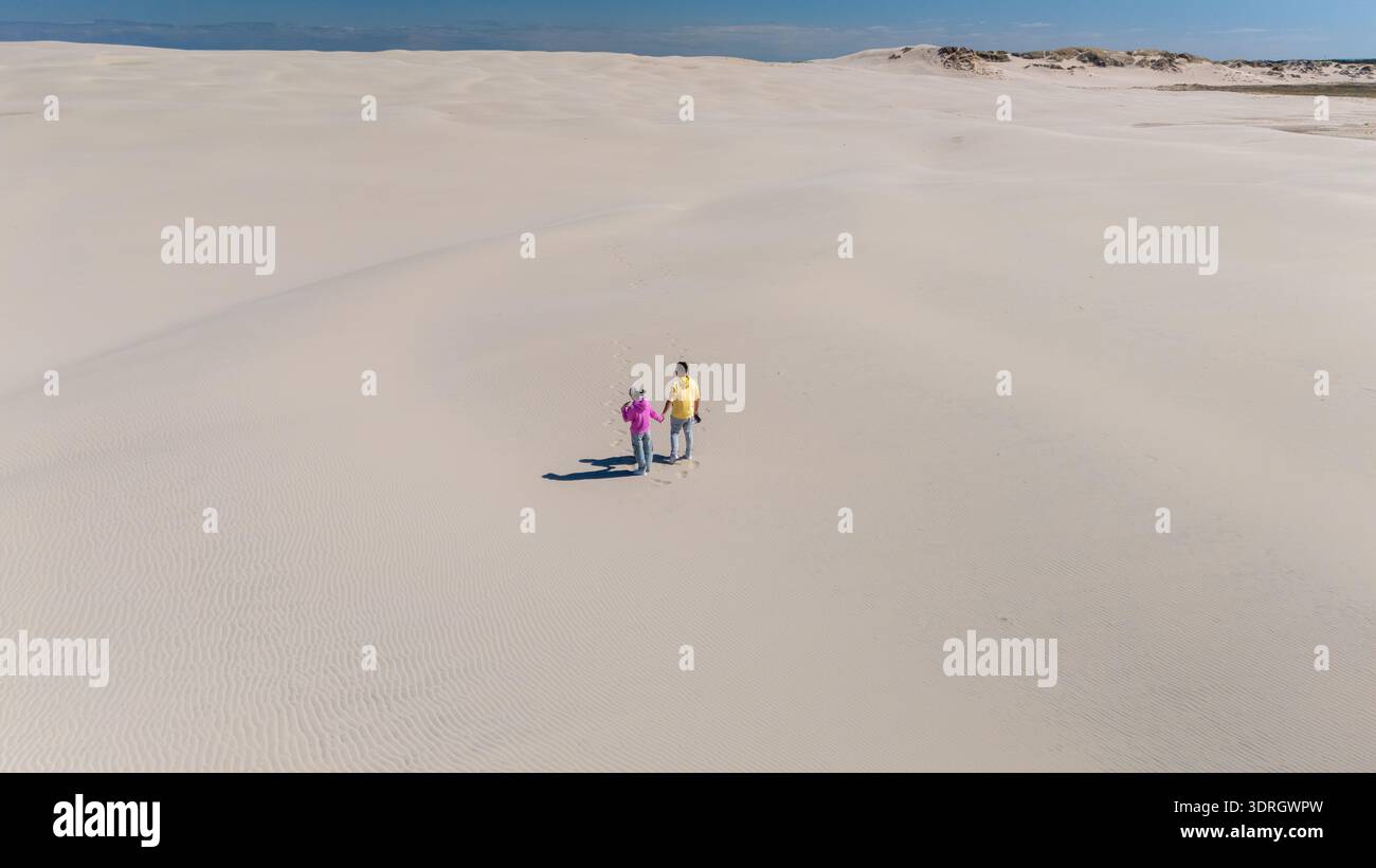 Couple marchant main dans la main sur une plage de sable sereine au Danemark sous un ciel bleu vif Banque D'Images