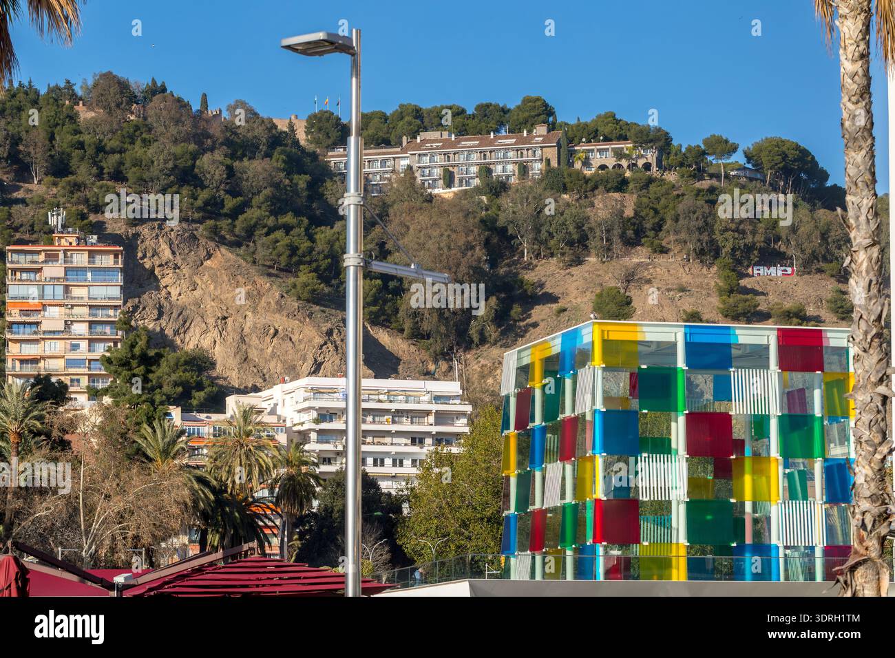 Malaga, Espagne – 10 février 2020 : le cube de verre coloré du musée du Centre Pompidou se dresse devant la colline Gibralfaro avec les murs historiques du château Banque D'Images