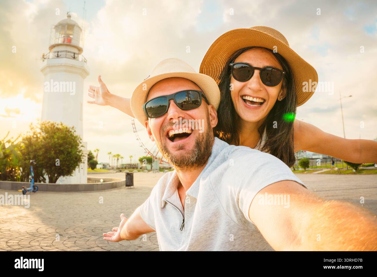 Jeune couple caucasien excité dans l'amour souriant prenant selfie pov à Batumi Boulevard avec phare emblématique et grande roue pendant l'heure d'or. Heureux Banque D'Images