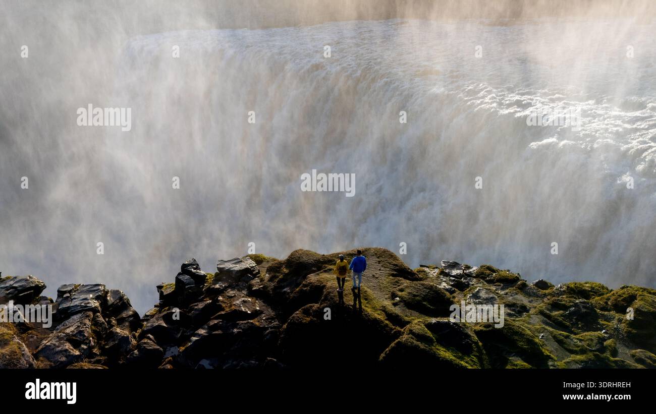 La cascade de Dettifoss descend en cascade les falaises rocheuses d'Islande, créant un spectacle époustouflant de puissance naturelle. Visiteurs enthousiastes a Banque D'Images