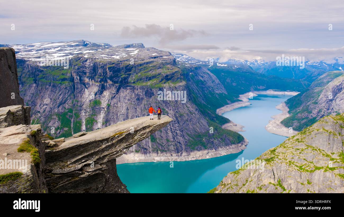 Les randonneurs se tiennent au bord de Trolltunga, en Norvège, s'émerveillant devant les falaises époustouflantes et les eaux bleues sereines du fjord norvégien. Banque D'Images