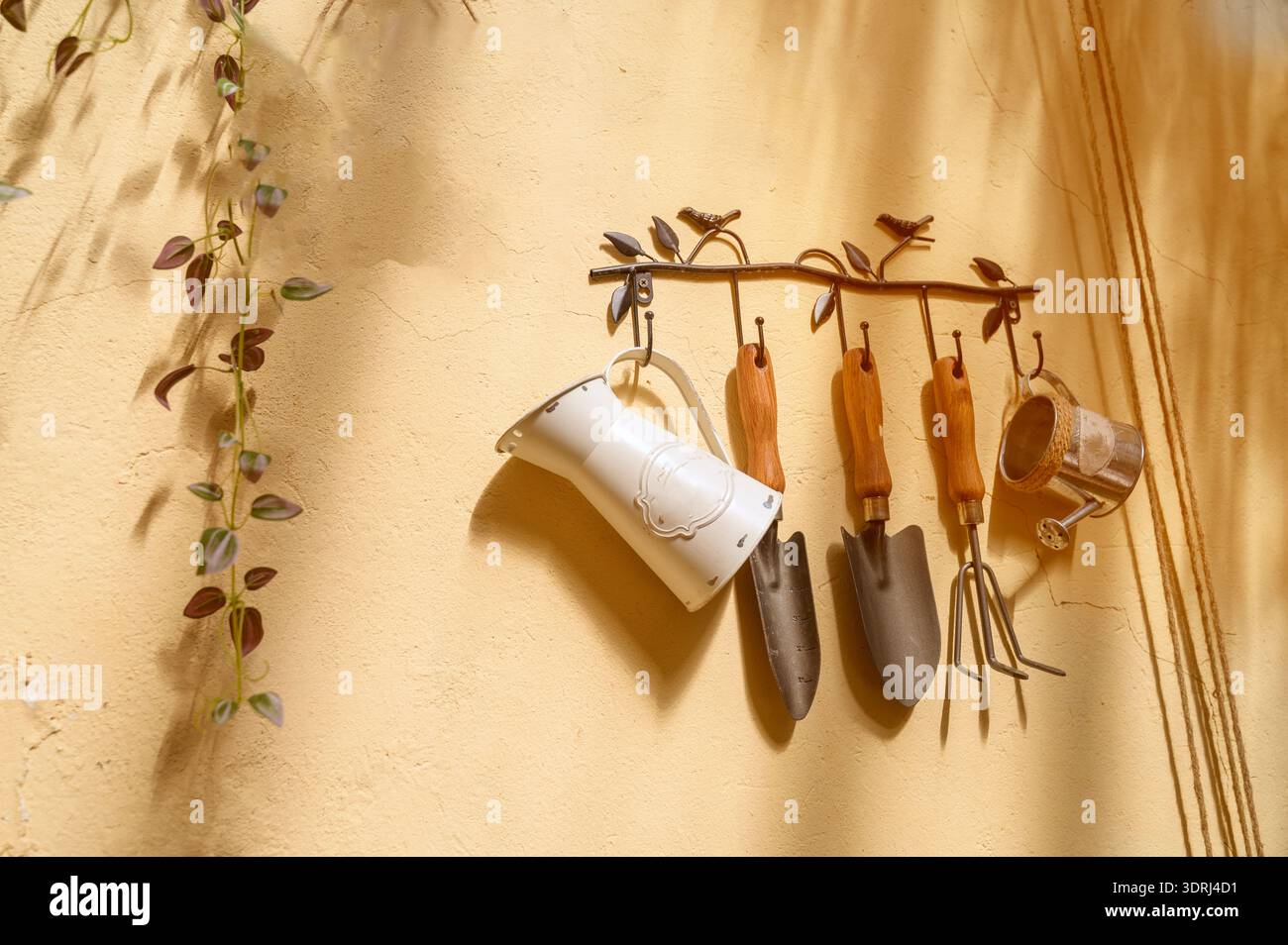 Des outils de jardinage vintage comme des truelles et un petit arrosoir accroché à un mur jaune. Concept de passe-temps de jardinage à la maison, soin des plantes domestiques et rouille Banque D'Images
