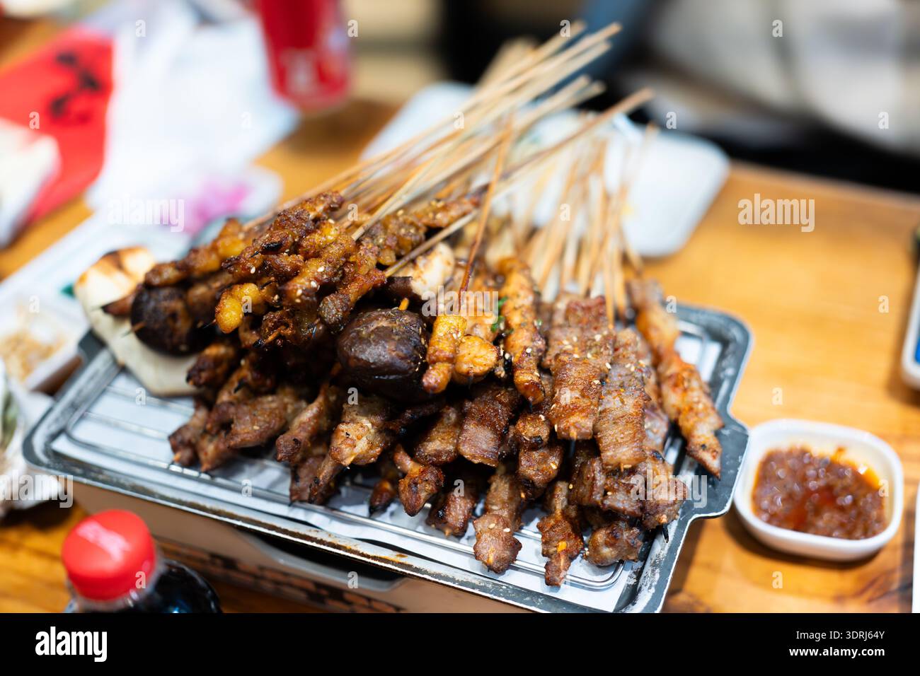 Brochettes satay indonésiennes grillées sur un plateau métallique avec sauce aux cacahuètes, servies sur une table en bois dans le restaurant Banque D'Images