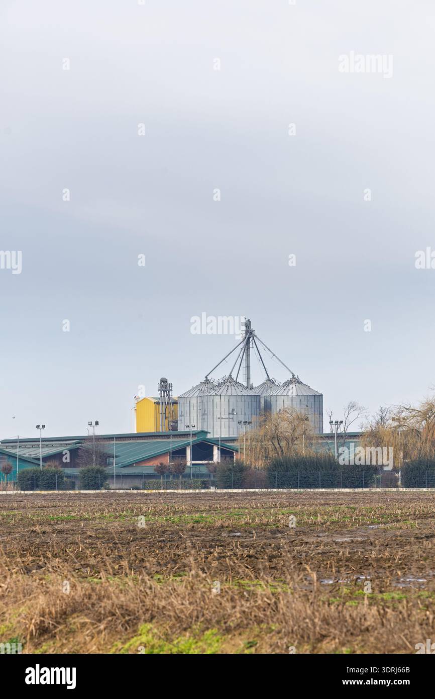 IVANKOVO, CROATIE, 02.14.2026:des silos à grains et une installation de stockage de métaux s’élèvent derrière un champ récolté sous un ciel couvert pâle, mettant en valeur la modernité Banque D'Images