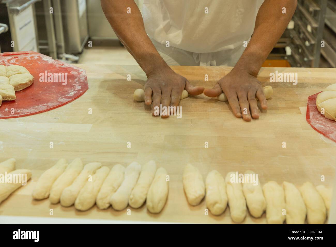 Boulanger façonnant la pâte en rouleaux sur un comptoir en bois dans un environnement de cuisine professionnel Banque D'Images