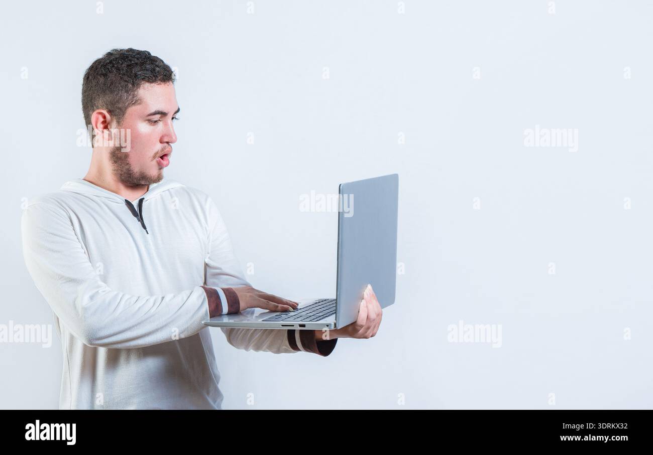 Gars surpris tenant et regardant une promotion sur l'écran d'ordinateur portable. Étonné bel homme debout à l'aide d'un ordinateur portable isolé Banque D'Images