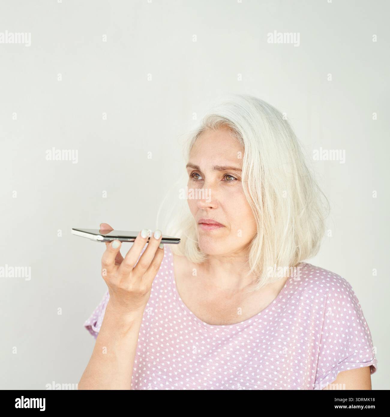 Femme mature caucasienne utilisant l'assistant vocal smartphone dans une tenue décontractée avec Banque D'Images