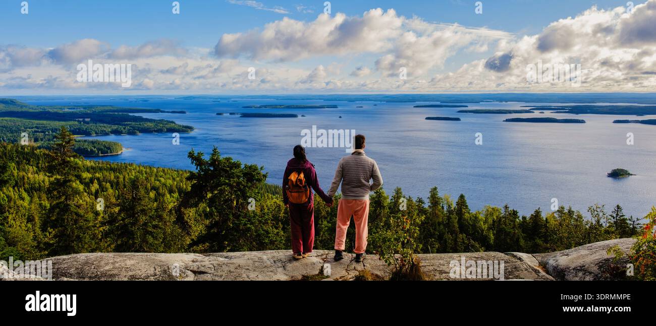 Deux randonneurs se tiennent sur une falaise rocheuse surplombant une vue imprenable sur le parc national de Koli en Finlande. Le vaste lac reflète Banque D'Images